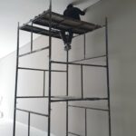 Profissional sobre andaime realizando acabamento e pintura interna de ambiente comercial em São Paulo