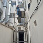 Técnico em andaime tubular realizando manutenção em unidade externa de ar-condicionado